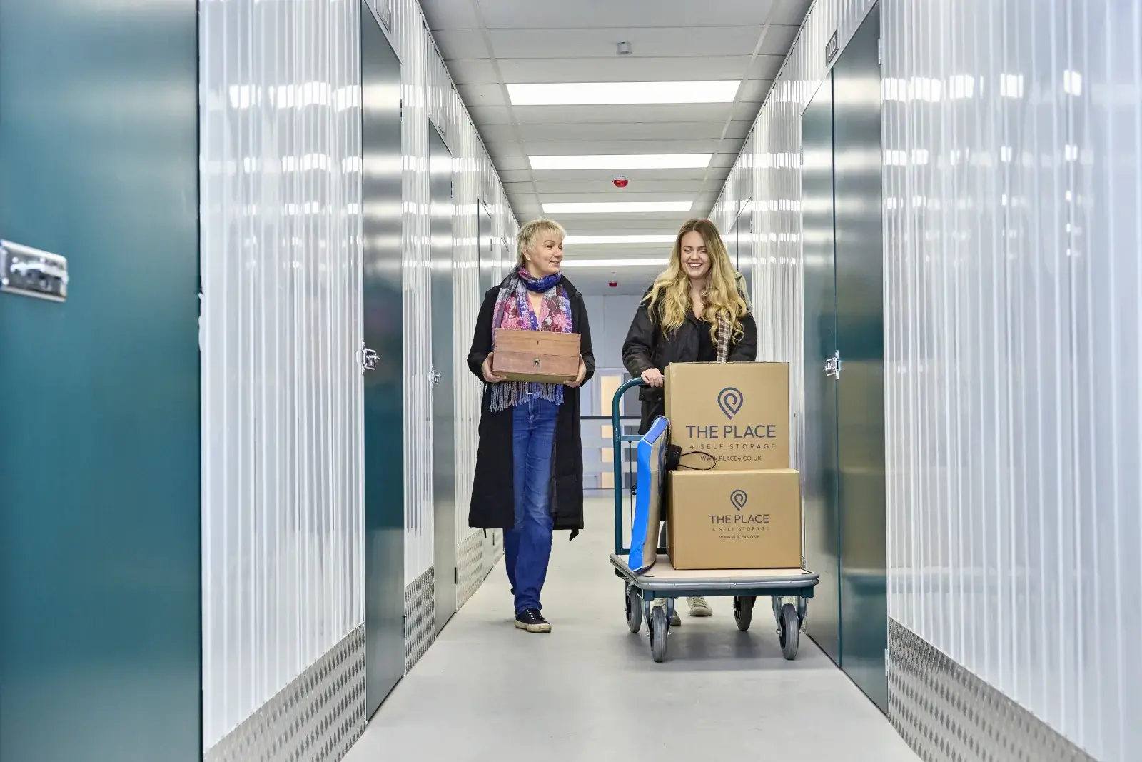 the-place-4-self-storage-customers-move-down-corridor-with-loaded-trolley-and-personal-items-1600x1067