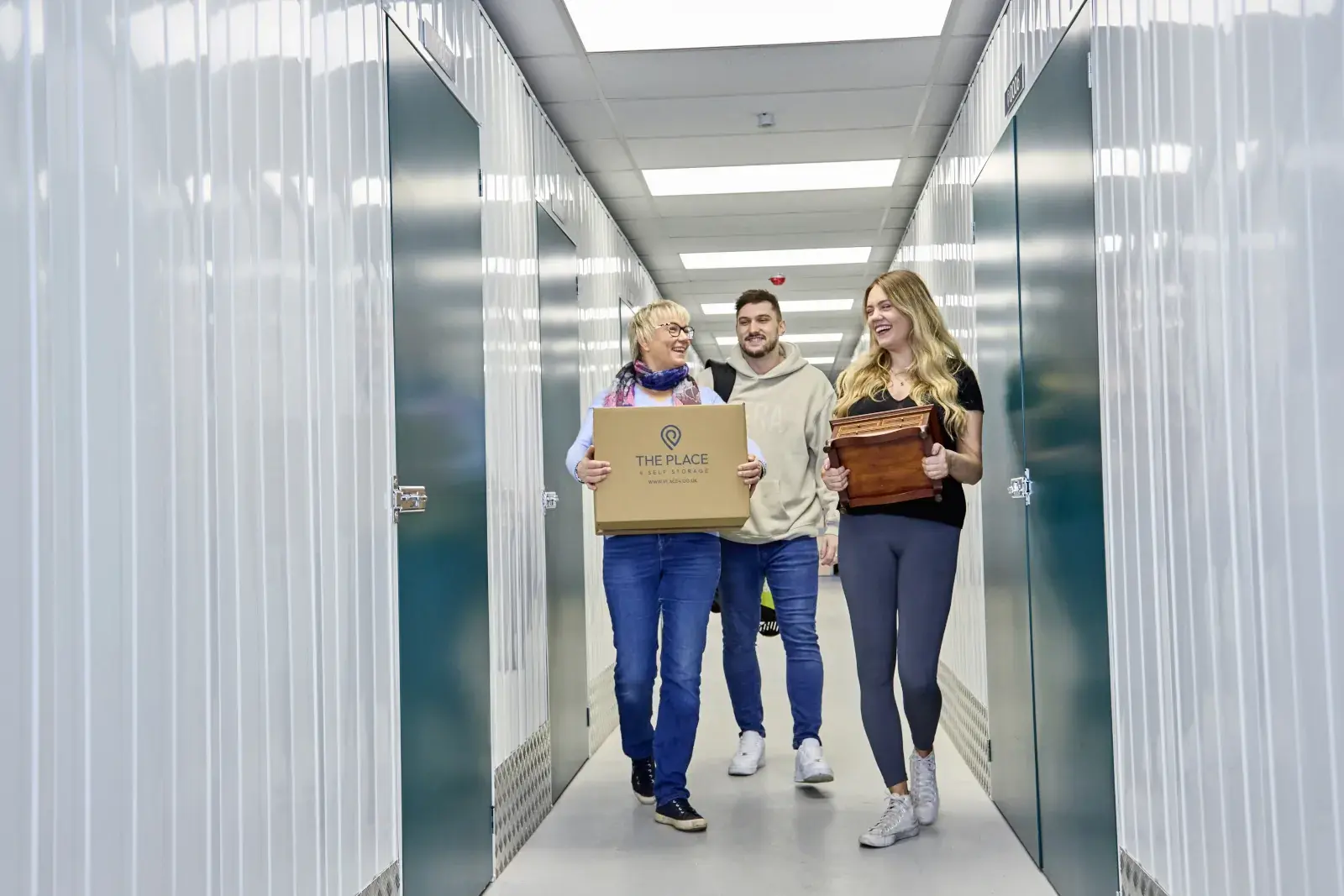 the-place-4-self-storage-family-carrying-possessions-down-corridor-to-secure-lock-up-unit-1600x1067
